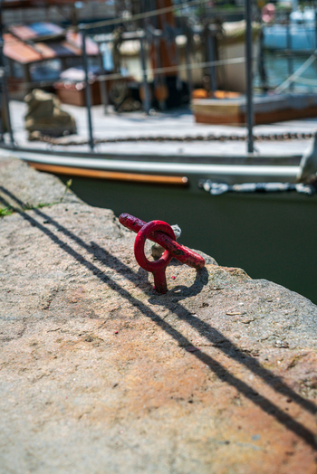 View of a red metal mooring ring on a weathered stone quay with a boat docked in the background at Charlestown Harbour in Charlestown Cornwall United Kingdom. View of a red metal mooring ring on a weathered stone quay with a boat docked in the background at Charlestown Harbour in Charlestown Cornwall United Kingdom.