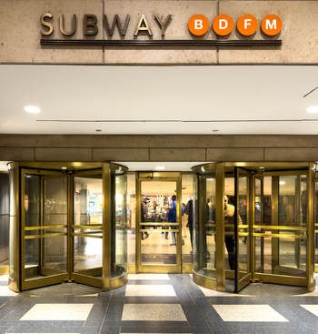 View of the entrance to a subway station featuring revolving brass doors and signs for the B D F and M lines New York New York United States. View of the entrance to a subway station featuring revolving brass doors and signs for the B D F and M lines New York New York United States.