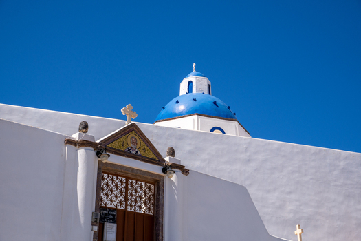 View of the traditional white architecture and iconic blue dome of a Greek Orthodox church against a clear sky in Fira Greece. View of the traditional white architecture and iconic blue dome of a Greek Orthodox church against a clear sky in Fira Greece.