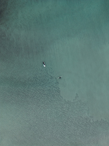 Aerial view of a person on a surfboard and a swimmer in the clear turquoise waters of the Lofoten islands in Svolvaer Nordland Norway.