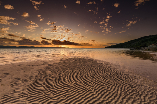 View of Quaranup Beach at sunset with rippled sand patterns calm water and a warm golden sky over the horizon in Vancouver Peninsula Western Australia Australia. View of Quaranup Beach at sunset with rippled sand patterns calm water and a warm golden sky over the horizon in Vancouver Peninsula Western Australia Australia.