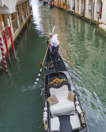 Venice Italy 21 September 2026 View of a gondolier rowing a traditional black gondola through a narrow canal with historic buildings and red and white mooring poles visible. Venice Italy 21 September 2026 View of a gondolier rowing a traditional black gondola through a narrow canal with historic buildings and red and white mooring poles visible.