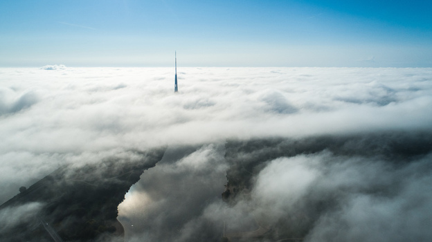 Aerial view of the Riga Radio and TV Tower rising above a thick sea of clouds with a river visible below in Riga Latvia. Aerial view of the Riga Radio and TV Tower rising above a thick sea of clouds with a river visible below in Riga Latvia.