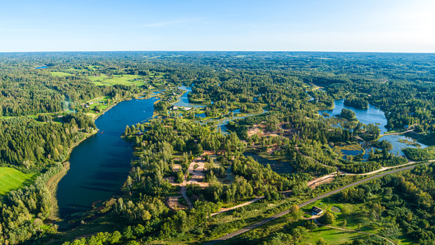 Aerial view of a winding lake surrounded by dense green forests and scattered trees under a clear blue sky in Latvia. Aerial view of a winding lake surrounded by dense green forests and scattered trees under a clear blue sky in Latvia.