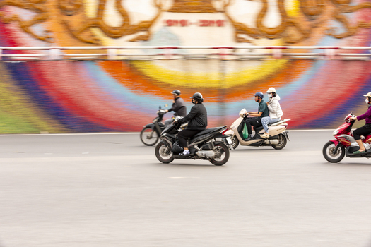 Hanoi Vietnam 11 November 2025 View of people riding motorbikes past the colorful Ceramic Mosaic Mural in the city streets.