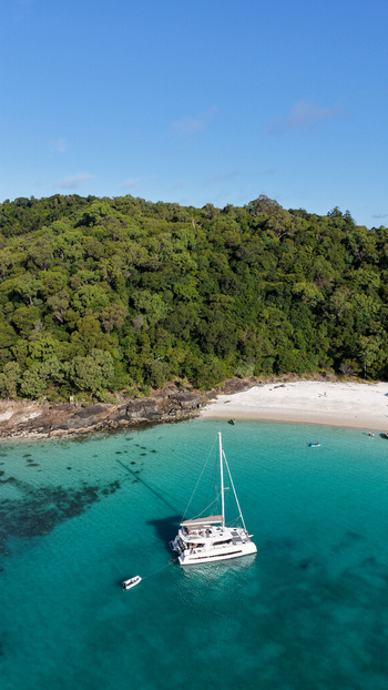 Aerial view of a catamaran anchored in the turquoise waters of Whitehaven Beach surrounded by lush tropical forest and white sand in Whitsundays Queensland Australia.