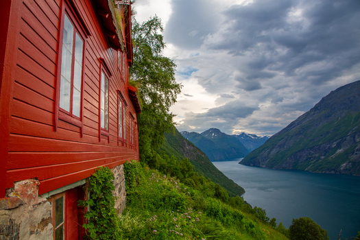 View of the historic Smage mountain farm with traditional red wooden architecture overlooking the Geirangerfjord surrounded by steep mountains in Geiranger More og Romsdal Norway.