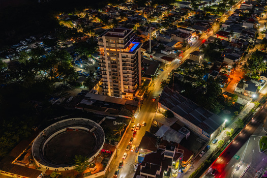 Aerial view of Plaza De Toros La Paloma Bull Ring illuminated at night next to a high rise building with a rooftop pool amidst city streets in Puerto Vallarta Jalisco Mexico.