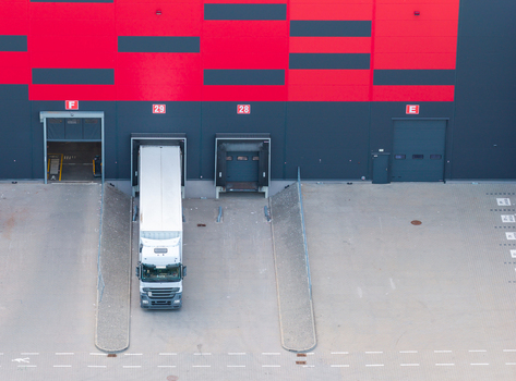 Aerial view of a logistics warehouse loading dock with a semi truck parked at bay 29 featuring red and black exterior walls in Kowale Pomeranian Voivodeship Poland. Aerial view of a logistics warehouse loading dock with a semi truck parked at bay 29 featuring red and black exterior walls in Kowale Pomeranian Voivodeship Poland.