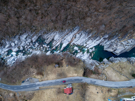 Aerial view of the turquoise Verzasca river flowing through the smooth granite rocks of Valle Verzasca near a winding road and a house with a red roof Verzasca Ticino Switzerland. Aerial view of the turquoise Verzasca river flowing through the smooth granite rocks of Valle Verzasca near a winding road and a house with a red roof Verzasca Ticino Switzerland.