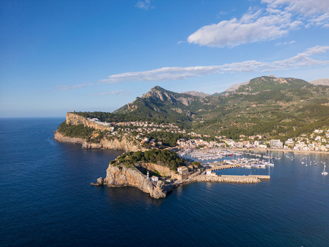 Aerial view of Port de Soller harbor with white boats and the lighthouse on rocky cliffs against the Tramuntana mountains Port de Soller Balearic Islands Spain.