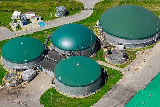 Aerial view of a biogas plant featuring large green domed storage tanks for fermented mass surrounded by paved access roads and grassy areas Poland.