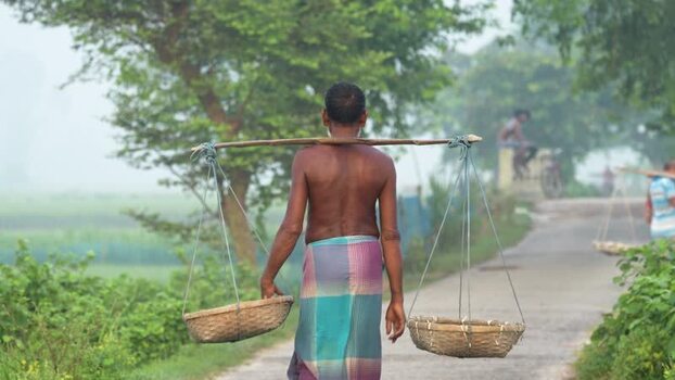 View of a man carrying baskets on a yoke Bangladesh.