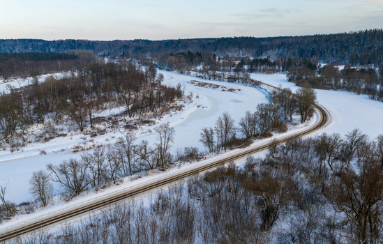 Aerial view of a frozen river winding through a snow covered winter forest with bare trees and a curved road in Lithuania. Aerial view of a frozen river winding through a snow covered winter forest with bare trees and a curved road in Lithuania.