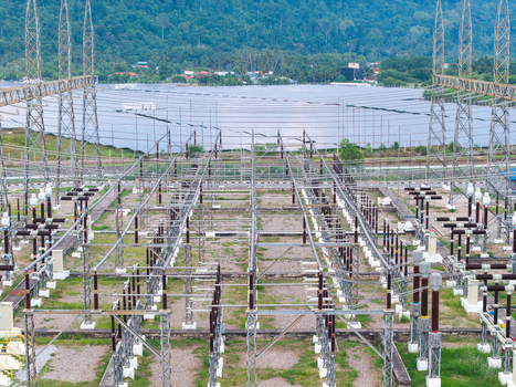 Aerial view of a high voltage transmission substation with metal towers and electrical equipment featuring a solar panel farm in the background Central Seberang Perai Penang Malaysia. Aerial view of a high voltage transmission substation with metal towers and electrical equipment featuring a solar panel farm in the background Central Seberang Perai Penang Malaysia.