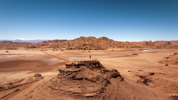 Aerial view of the arid desert landscape with a person standing on a rocky outcrop under a clear blue sky in Tolar Grande Salta Province Argentina. Aerial view of the arid desert landscape with a person standing on a rocky outcrop under a clear blue sky in Tolar Grande Salta Province Argentina.