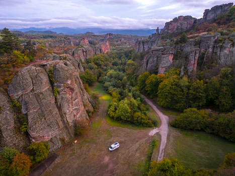 Aerial view of the dramatic Belogradchik Rocks with unique red sandstone formations lush autumn forests and a small camper van parked on a dirt path in Belogradchik Vidin Bulgaria. Aerial view of the dramatic Belogradchik Rocks with unique red sandstone formations lush autumn forests and a small camper van parked on a dirt path in Belogradchik Vidin Bulgaria.