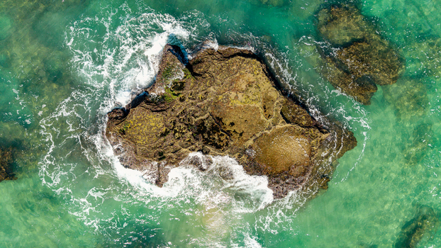 Aerial view of a rugged rocky reef surrounded by crystal clear turquoise ocean water and crashing white waves near Hartenbos Mossel Bay Western Cape South Africa. Aerial view of a rugged rocky reef surrounded by crystal clear turquoise ocean water and crashing white waves near Hartenbos Mossel Bay Western Cape South Africa.
