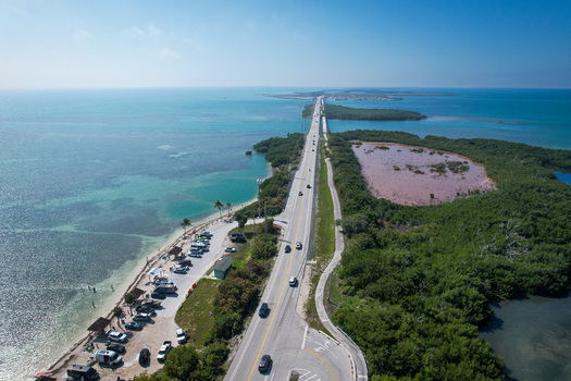 Aerial view of The Overseas Highway stretching across turquoise waters and lush green mangroves with cars parked along the beach in Key Largo Florida United States. Aerial view of The Overseas Highway stretching across turquoise waters and lush green mangroves with cars parked along the beach in Key Largo Florida United States.