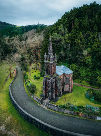 Aerial view of the mystical Capela de Nossa Senhora das Vit&oacute;rias nestled in a vibrant green valley a winding road leading to its gothic facade S&atilde;o Miguel Island Azores Portugal.
