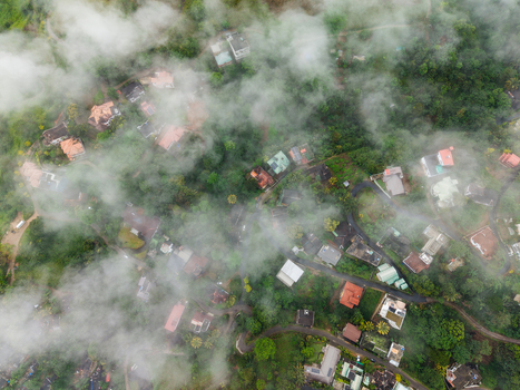 Aerial view of houses and winding roads nestled in a lush green forest partially covered by thick white clouds Kandy Central Province Sri Lanka. Aerial view of houses and winding roads nestled in a lush green forest partially covered by thick white clouds Kandy Central Province Sri Lanka.