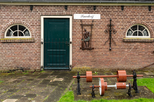 View of the Dutch Steam Engine Museum smithy featuring a brick facade green door and vintage industrial pulleys in Medemblik Noord Holland Netherlands. View of the Dutch Steam Engine Museum smithy featuring a brick facade green door and vintage industrial pulleys in Medemblik Noord Holland Netherlands.