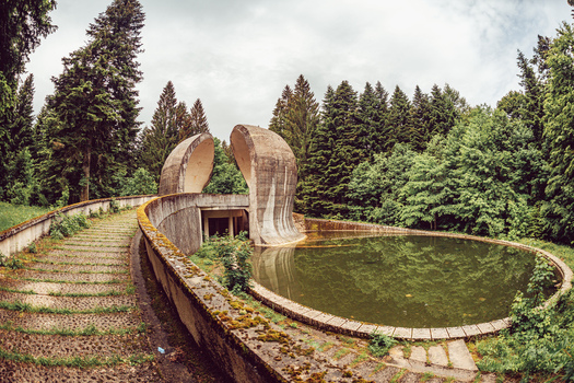 View of the Korcanica Memorial Monument with its brutalist concrete wings and a circular pool in a dense forest Sanski Most Federation of Bosnia Bosnia and Herzegovina. View of the Korcanica Memorial Monument with its brutalist concrete wings and a circular pool in a dense forest Sanski Most Federation of Bosnia Bosnia and Herzegovina.