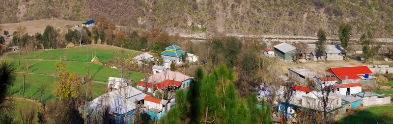 Aerial view of a rural village in the Galiyat region featuring colorful rooftops green agricultural fields and surrounding mountainous terrain in Galiyat Pakistan.