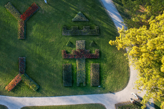 Aerial view of colorful flower beds shaped like a castle and letters in a green park with gravel paths and people walking Morges Vaud Switzerland. Aerial view of colorful flower beds shaped like a castle and letters in a green park with gravel paths and people walking Morges Vaud Switzerland.