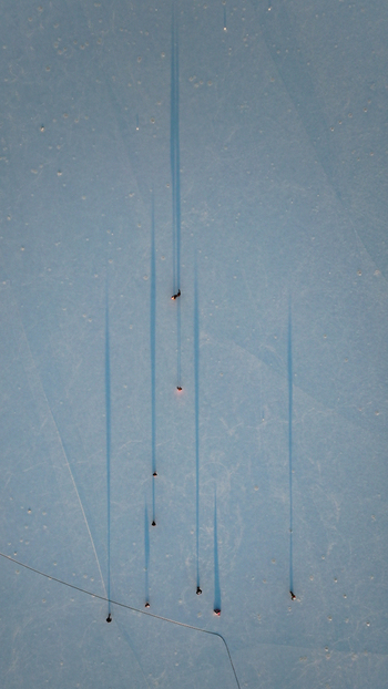 Aerial view of ice skaters on snow covered frozen lake their shadows stretching long and blue Les Rousses Bourgogne Franche Comté France. Aerial view of ice skaters on snow covered frozen lake their shadows stretching long and blue Les Rousses Bourgogne Franche Comté France.