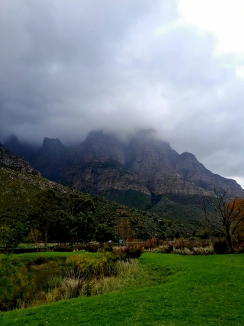 View of the rugged peaks of the Western Cape mountains partially obscured by low hanging clouds above a lush green valley with trees and grass in Montagu Western Cape South Africa.