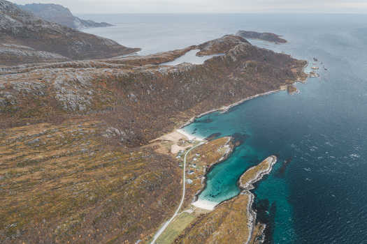 Aerial view of the rugged coastline of Senja featuring turquoise waters sandy beaches rocky terrain and a winding road in Senja Troms Norway.