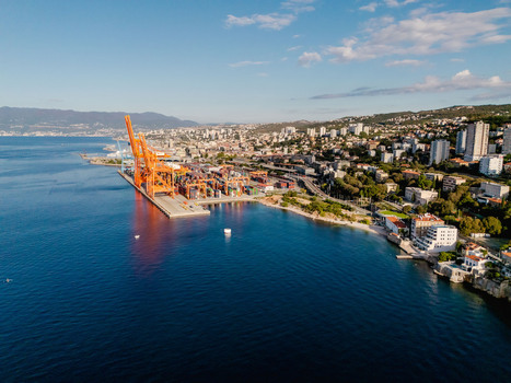 Aerial view of the industrial port of Rijeka featuring large orange cranes shipping containers and the coastal city landscape along the Adriatic Sea in Rijeka Primorje Gorski Kotar Croatia.