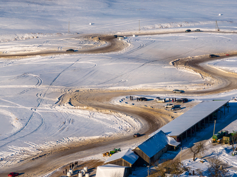 Aerial view of a winding ice racing track in a snowy landscape with cars driving and people gathered near a long building Moletai Utena County Lithuania.