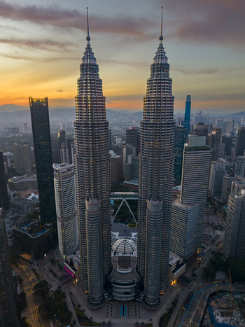 Kuala Lumpur Malaysia 11 March 2026 Aerial view of the Petronas Twin Towers towering over the city skyline during a vibrant sunset with orange and purple clouds.