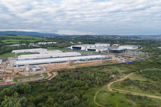 Aerial view of a large data center complex under construction featuring expansive industrial buildings surrounding green fields and heavy machinery United Kingdom.