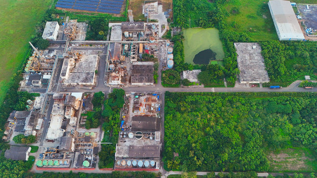 Aerial view of an industrial manufacturing plant featuring various factory buildings storage tanks and infrastructure surrounded by lush green vegetation in Olpad Gujarat India. Aerial view of an industrial manufacturing plant featuring various factory buildings storage tanks and infrastructure surrounded by lush green vegetation in Olpad Gujarat India.