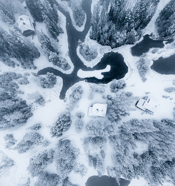 Aerial view of a winding river flowing through a snow covered forest landscape with scattered houses in Latvia. Aerial view of a winding river flowing through a snow covered forest landscape with scattered houses in Latvia.