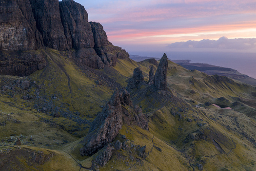 Aerial view of The Storr rock formations and green grassy slopes under a pink sunset sky in Isle of Skye Scotland United Kingdom. Aerial view of The Storr rock formations and green grassy slopes under a pink sunset sky in Isle of Skye Scotland United Kingdom.