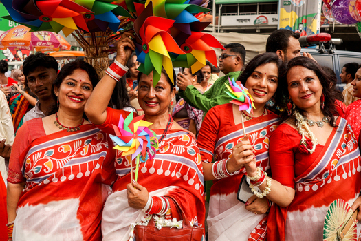 Dhaka Bangladesh 13 April 2026 View of joyful women in striking red and white saris holding vibrant pinwheels amidst a festive crowd their smiles reflecting the colorful celebration.