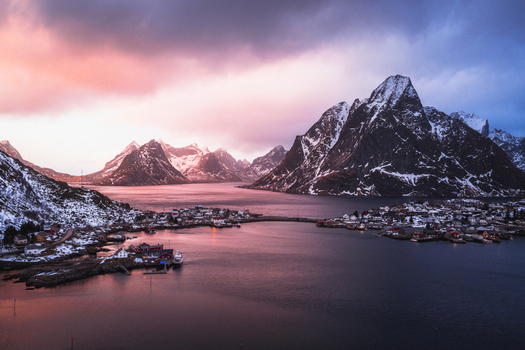 Aerial view of the dramatic snow dusted peaks embracing the tranquil waters dotted with charming villages in the golden light Reinebringen Nordland Norway.