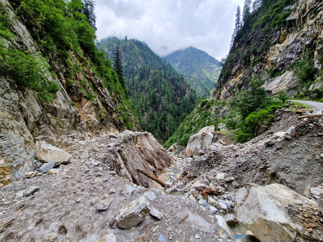 View of the rugged mountain path in Malana showing signs of a recent landslide with rocky debris steep cliffs and lush pine forests in Malana Himachal Pradesh India.