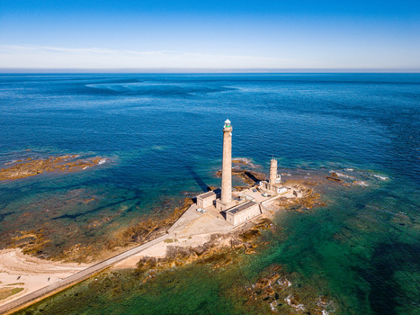 Aerial view of Gatteville Lighthouse standing on a rocky peninsula surrounded by the clear blue waters of the English Channel in Gatteville le Phare Normandie France.