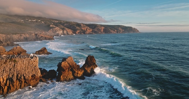 Aerial view of the rugged coastline of Lisbon with dramatic cliffs crashing waves and golden hour light hitting the rocky formations in Lisbon Lisbon Portugal. Aerial view of the rugged coastline of Lisbon with dramatic cliffs crashing waves and golden hour light hitting the rocky formations in Lisbon Lisbon Portugal.