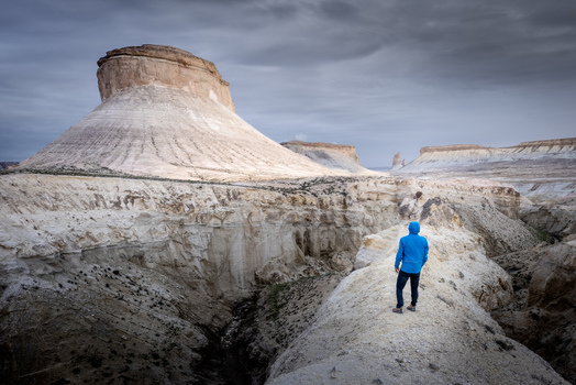 Aerial view of a person in a blue jacket standing on a rocky ridge overlooking the white limestone buttes and desert landscape of Mangistau Mangystau Region Kazakhstan.