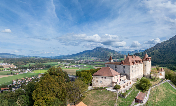 Aerial view of the historic Chateau de Gruyeres surrounded by lush green hills and the Swiss Alps in Gruyeres Fribourg Switzerland. Aerial view of the historic Chateau de Gruyeres surrounded by lush green hills and the Swiss Alps in Gruyeres Fribourg Switzerland.
