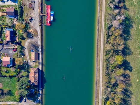 Aerial view of boats docked near houses and rowers gliding on the canal s emerald waters framed by lush greenery and earthy pathways Sausheim Grand Est France.
