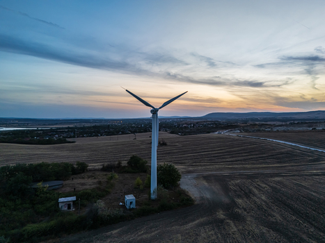 Aerial view of a wind turbine above harvested fields near Inota Hungary generating renewable electricity beneath a clouded sunset sky at twilight. Aerial view of a wind turbine above harvested fields near Inota Hungary generating renewable electricity beneath a clouded sunset sky at twilight.