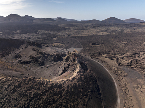 Aerial view of the volcanic landscape of Timanfaya National Park with rugged lava fields craters and arid terrain under a clear sky in Lanzarote Canarias Spain. Aerial view of the volcanic landscape of Timanfaya National Park with rugged lava fields craters and arid terrain under a clear sky in Lanzarote Canarias Spain.