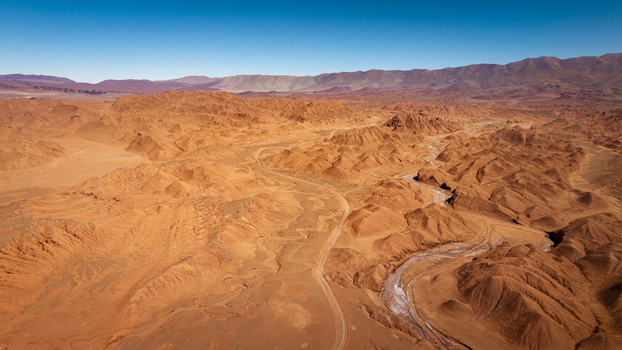 Aerial view of the arid desert landscape with winding dirt roads and dry riverbeds surrounded by rolling hills under a clear blue sky in Tolar Grande Salta Province Argentina. Aerial view of the arid desert landscape with winding dirt roads and dry riverbeds surrounded by rolling hills under a clear blue sky in Tolar Grande Salta Province Argentina.